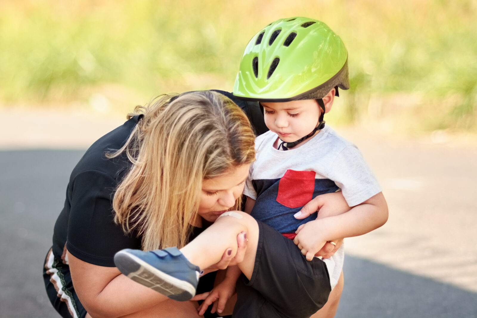 A mother tends to her son's scraped elbow while he wears a bike helmet.